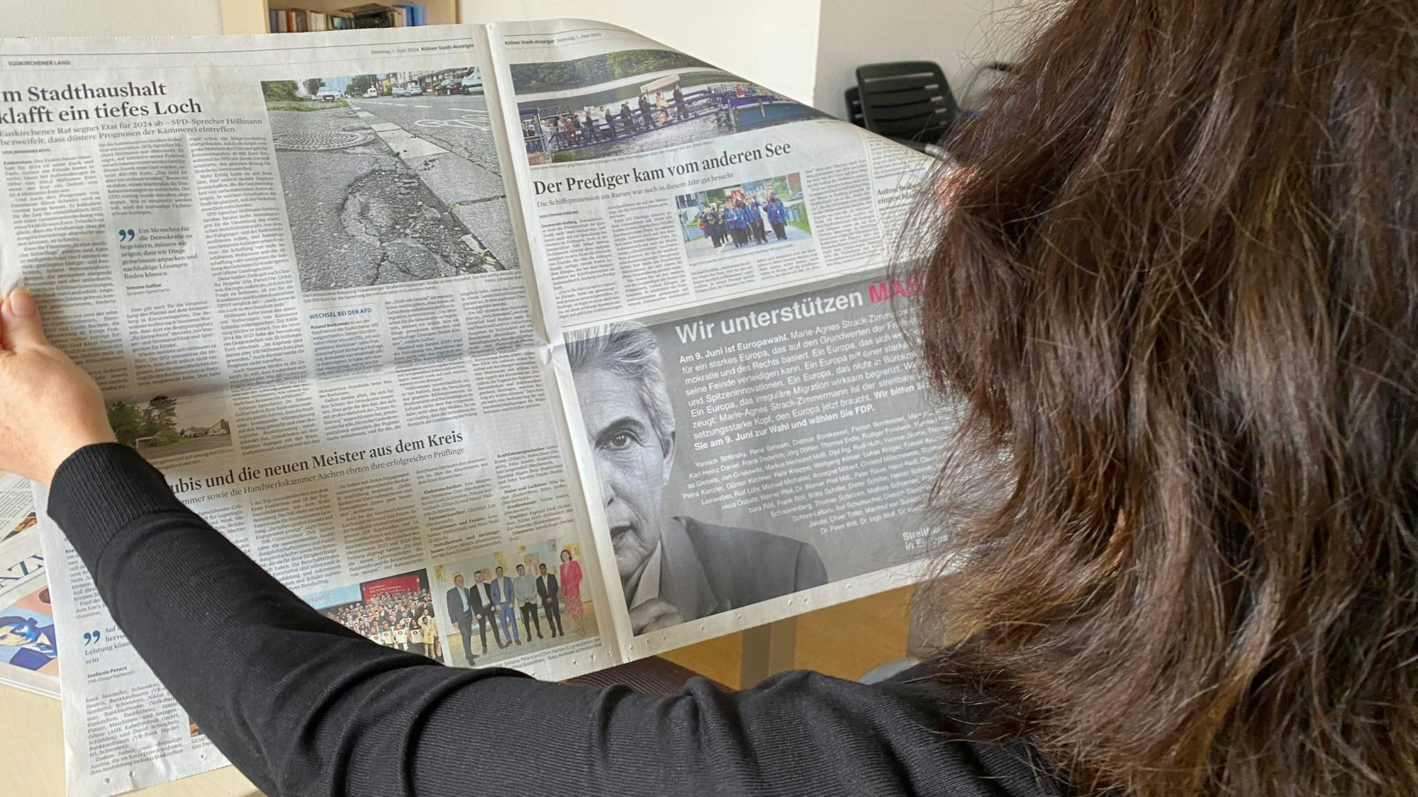 Eine Leserin hält eine Zeitung vor sich, auf der rechten Seite ist eine Wahlkampf-Anzeige der FDP zu sehen.