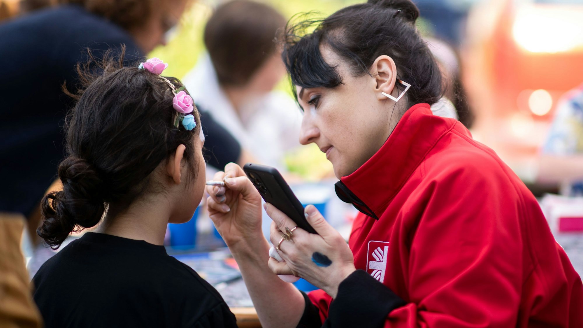 Das Bild zeigt eine Mitarbeiterin der Caritas, die ein Kind schminkt.