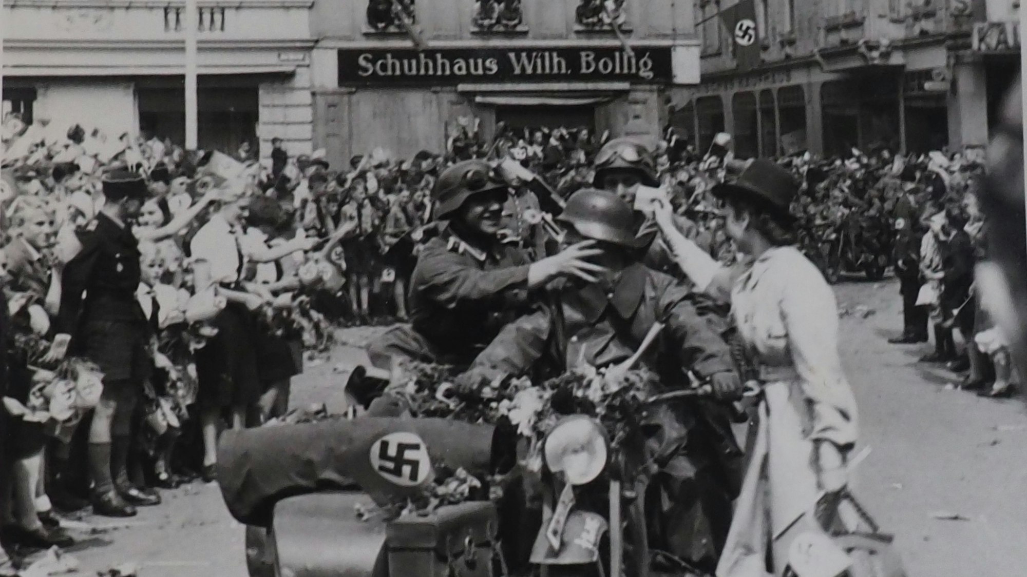 Soldaten auf einem Motorrad mit Beiwagen fahren auf den Euskirchener Marktplatz. Am Rand stehen jubelnde Menschen.