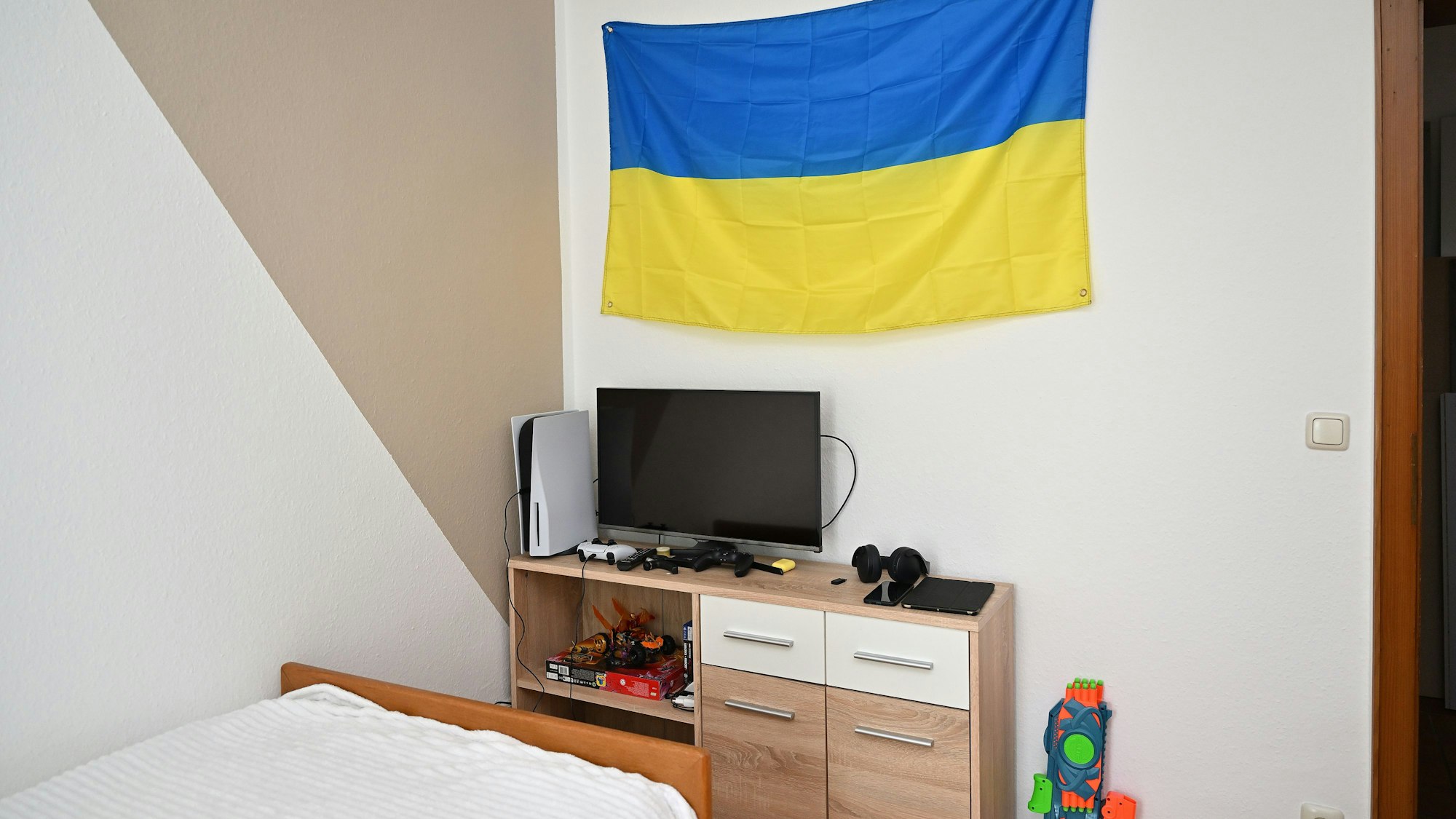 Ein Jugendzimmer mit Bett und Sideboard, darauf ein Bildschirm.