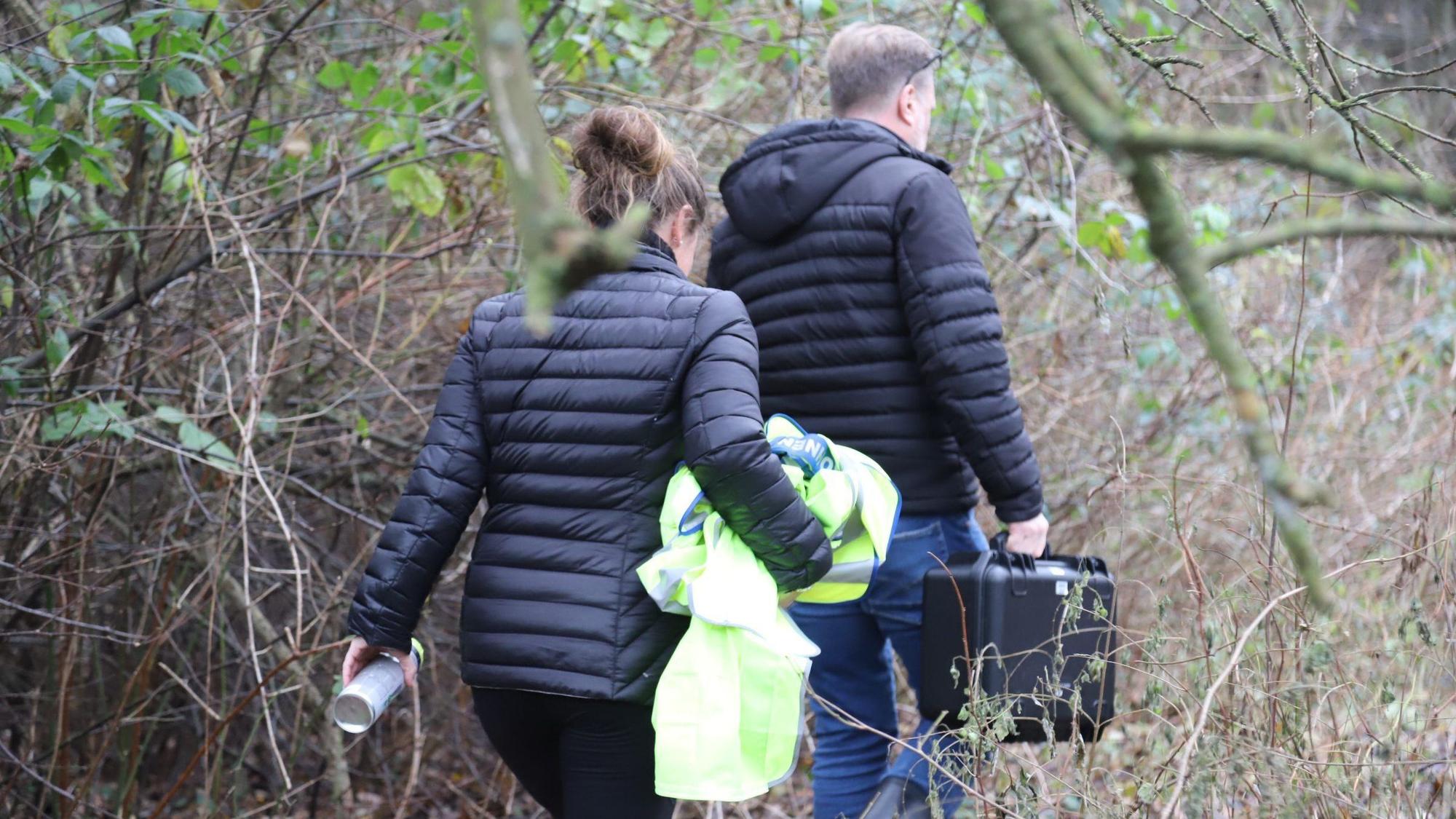 Beamte der Bielefelder Kriminalpolizei sind für die Spurensicherung auf dem Weg zu einer Waldfläche.