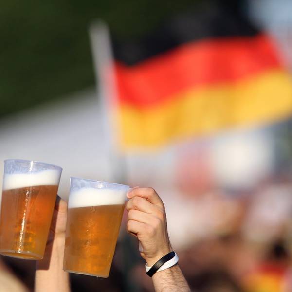 Zwei Bierbecher werden von Fußball-Fans vor einer Deutschland-Fahne in die Höhe gehalten. (Symbolbild)