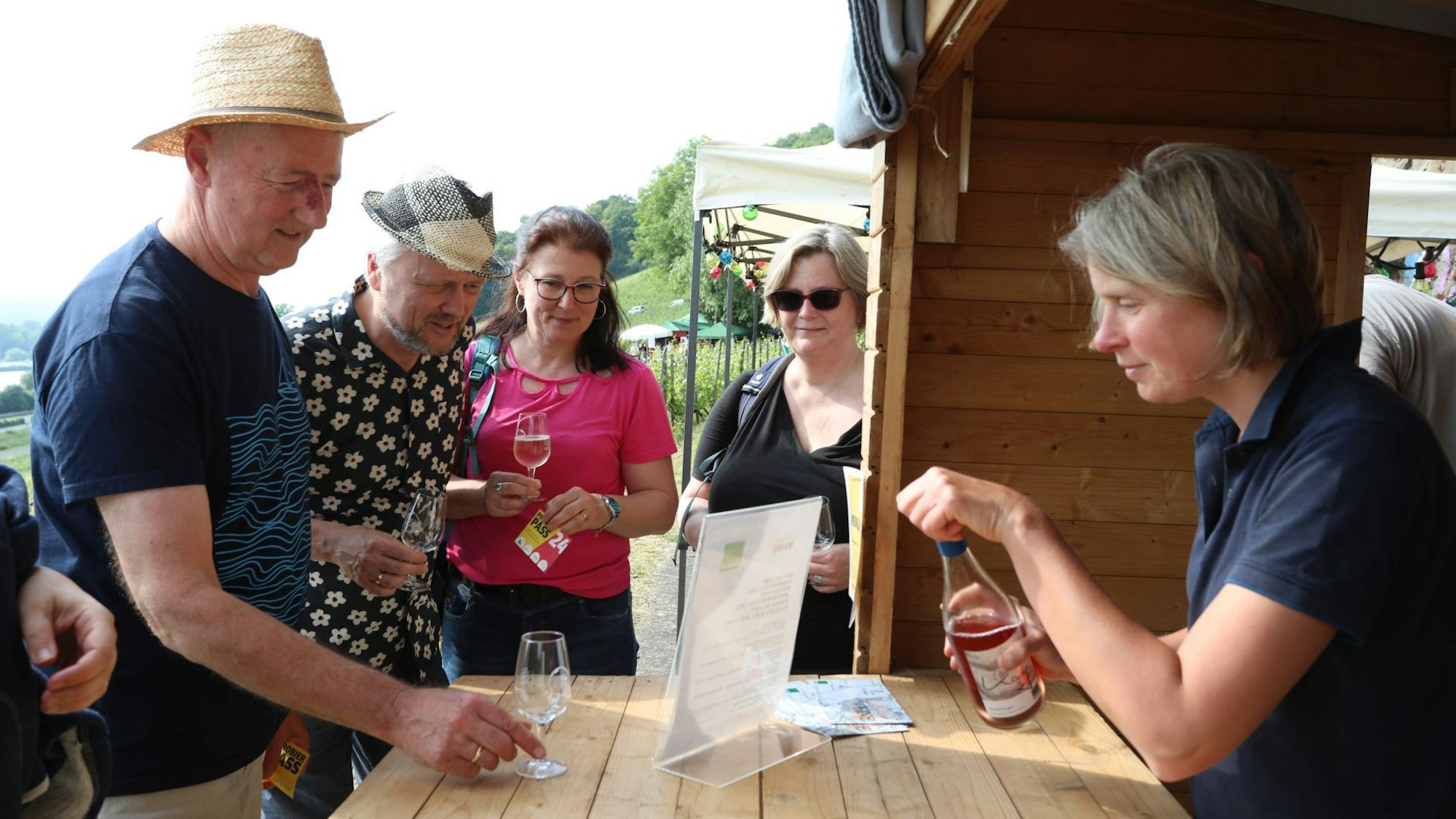 Menschen stehen an einem Holzbüdchen, mit Weingläsern in der Hand.