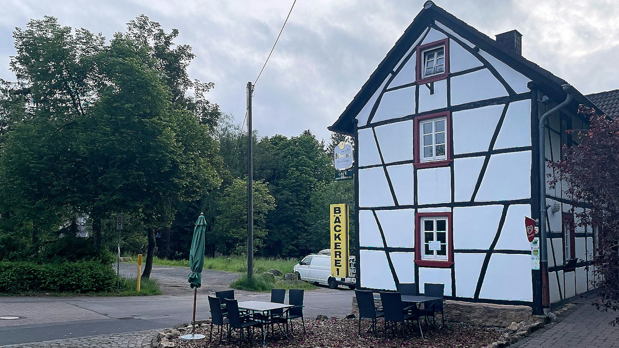 An einem Fachwerkhaus in Nettersheim ist an der linken Ecke eine gelbe Leuchtreklame mit der Aufschrift „Bäckerei“ angebracht.