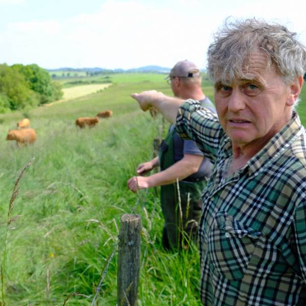 Der Landwirt Paul Milz deutet mit ausgestrecktem Arm auf die Weide, wo einige seiner Rinder stehen. Sein Kollege Marcel May steht neben ihm.