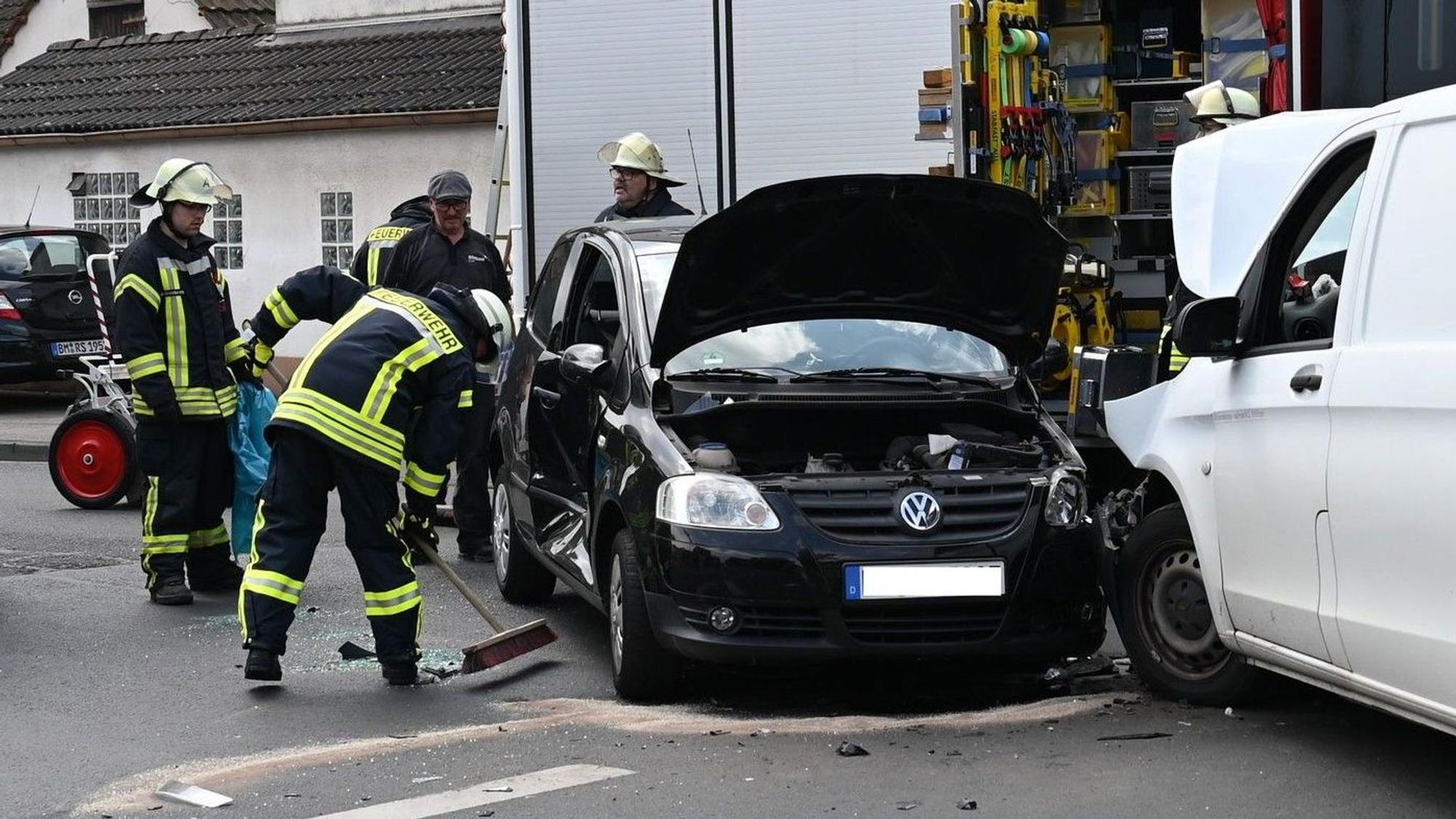 Das Bild zeigt zwei Autos die zusammengestoßen sind und Feuerwehrmänner, die auslaufende Flüssigkeiten abstreuen.
