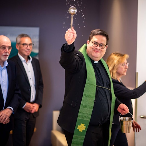 Das Bild zeigt unter anderem Pfarrer Tobias Hopmann, der Weihwasser im Raum verteilt.