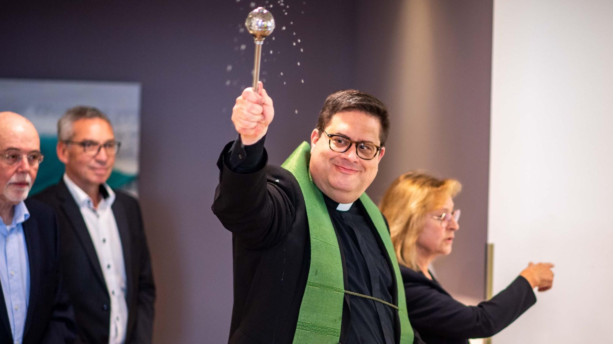 Das Bild zeigt unter anderem Pfarrer Tobias Hopmann, der Weihwasser im Raum verteilt.