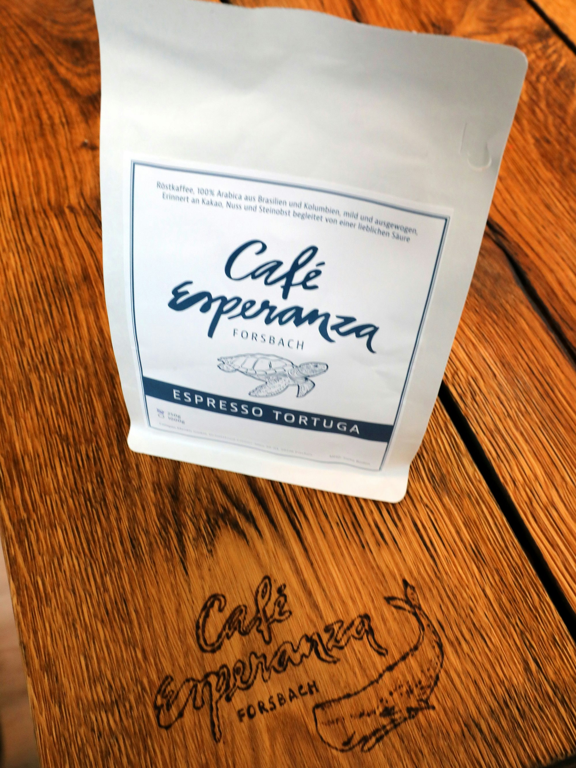 Eine Kaffee-Tüte mit der Aufschrift Café Esperanza Forsbach steht auf einem Holztisch, auf dem sich die gleiche Inschrift lesen lässt.