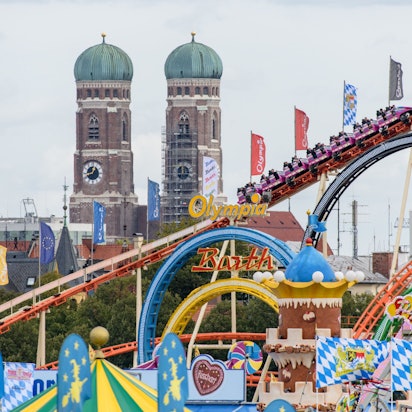 Bayern, München: Oktoberfestbesucher fahren 2018 in einer Achterbahn auf dem Oktoberfest auf der Theresienwiese. Im Hintergrund ist die Frauenkirche in der Münchner Altstadt zu sehen.