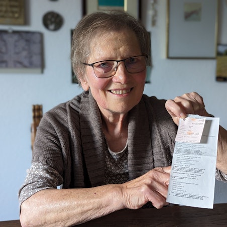 Eine Frau hält einen Busfahrschein und den Ausdruck einer Zahlungsaufforderung in den Händen.