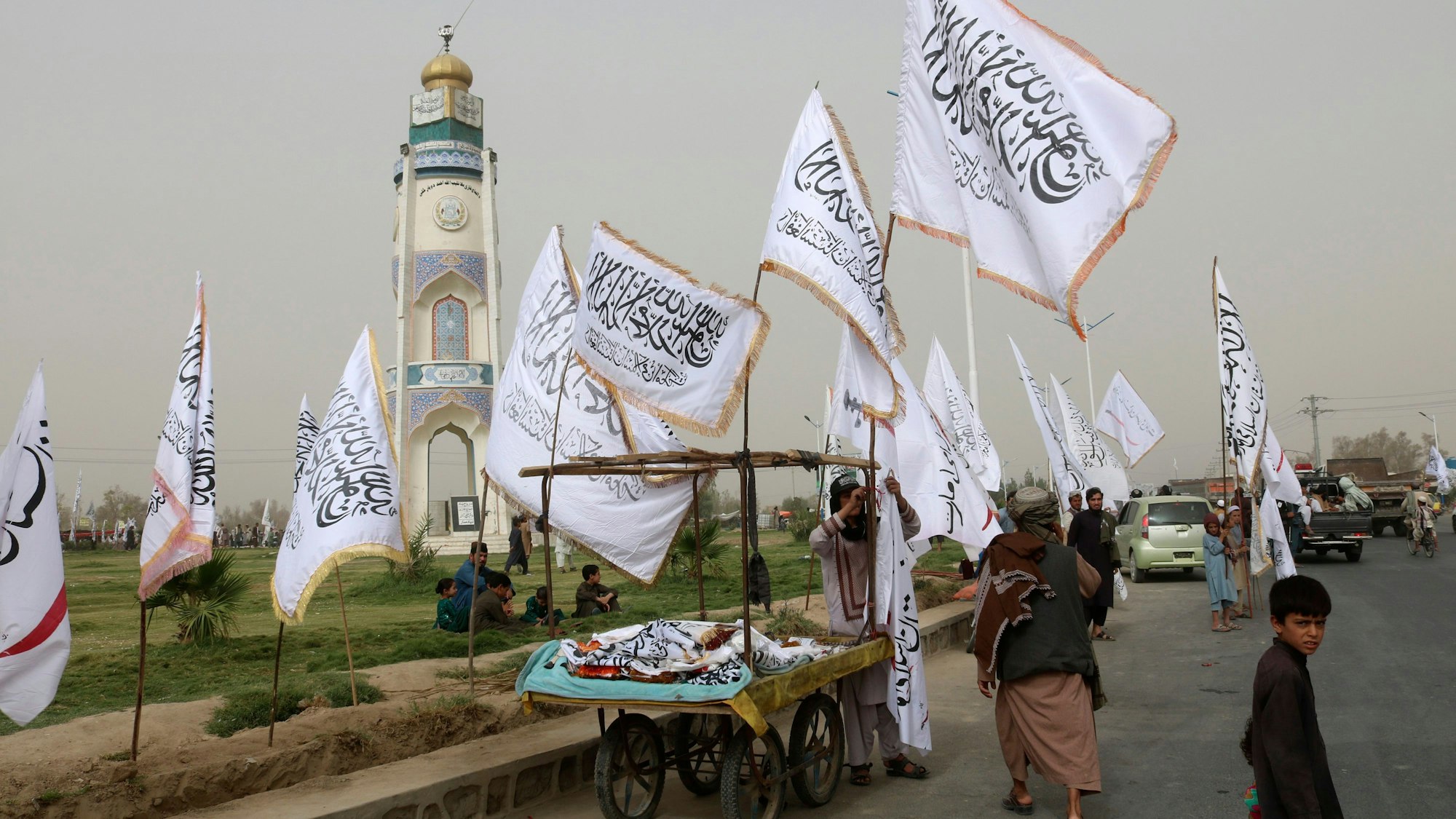 Ein afghanischer Mann und Kinder verkaufen während einer Feier zum zweiten Jahrestag des Abzugs der US-amerikanischen Truppen aus Afghanistan Taliban-Fahnen an Passanten.