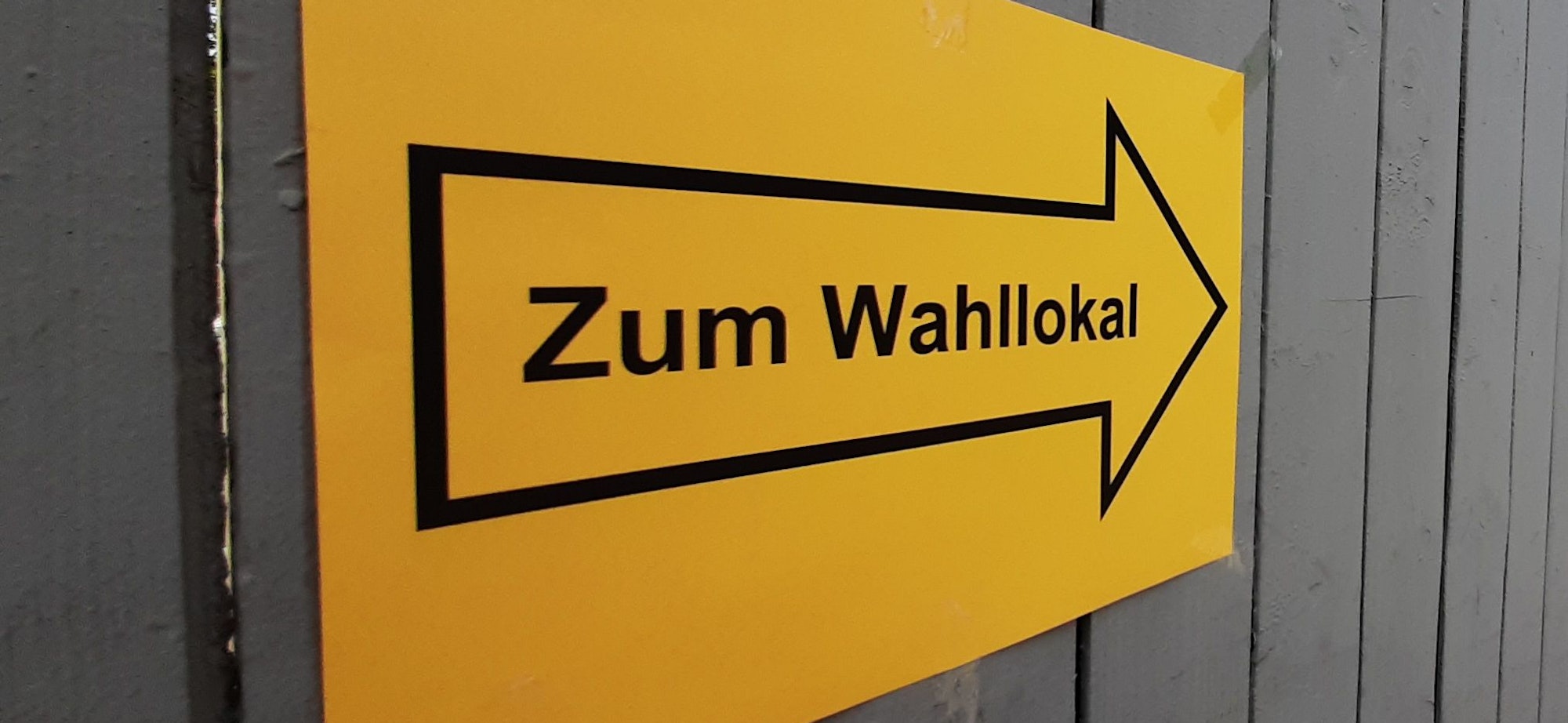 Ein Schild mit der Aufschrift „Zum Wahllokal“ hängt an einem Bretterzaun.