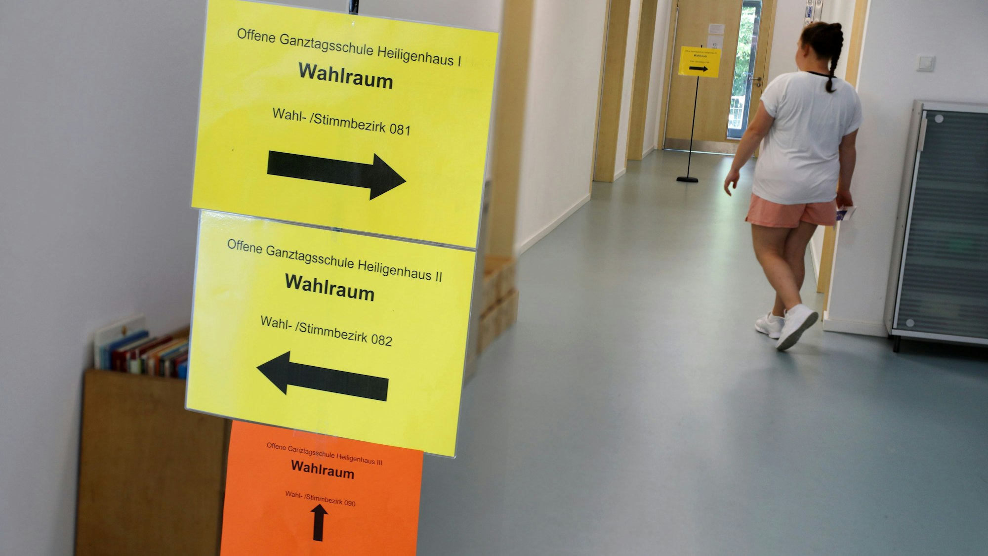 Eine junge Frau geht in einen Flur, an dem ein Schild den Weg zu einem Wahlraum ausweist.