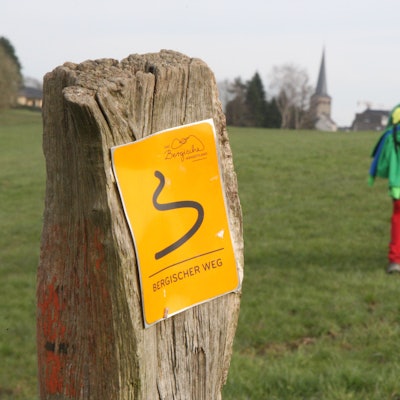 Zwei Kinder wandern auf dem Bergischen Weg in Richtung der Kirche von Neunkirchen.