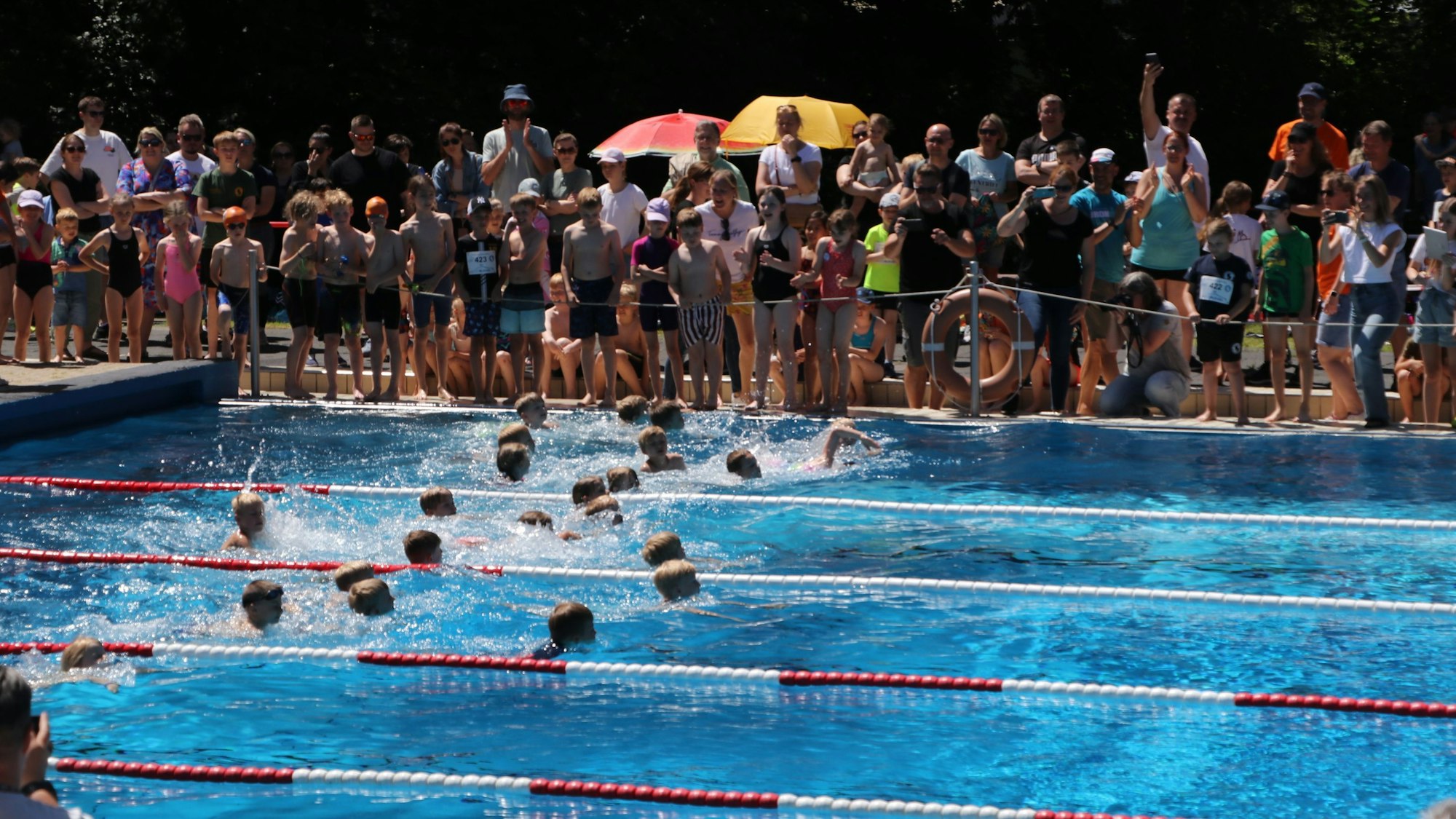 Auf dem Bild sind Kinder im Schwimmbecken und Zuschauer am Beckenrand zu sehen.