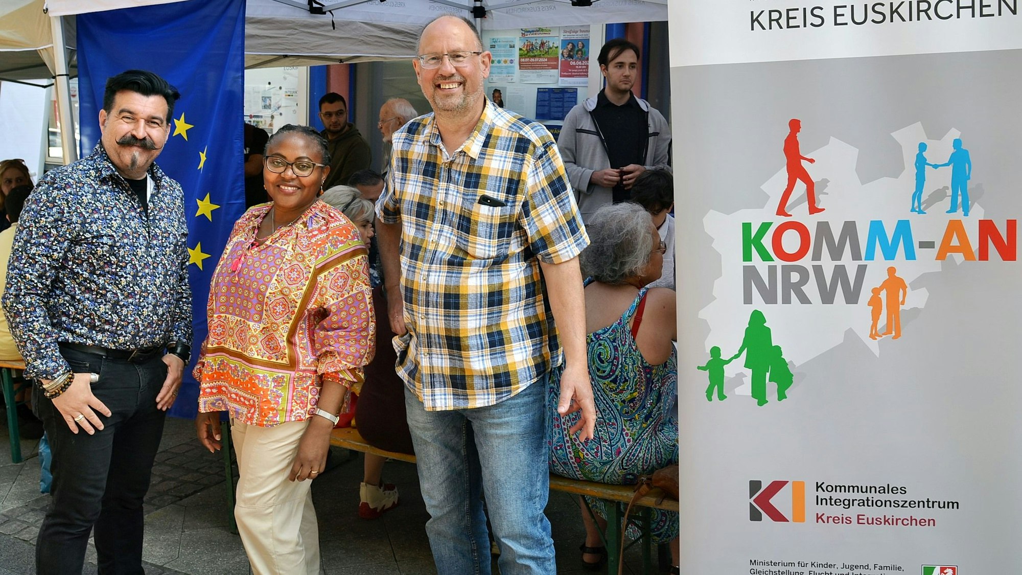 Robert Kuhlen (Kobiz), Epiphanie Uwimana und Norbert Weber stehen vor einem Pavillon der „Tafel der Demokratie“ in Euskirchen.