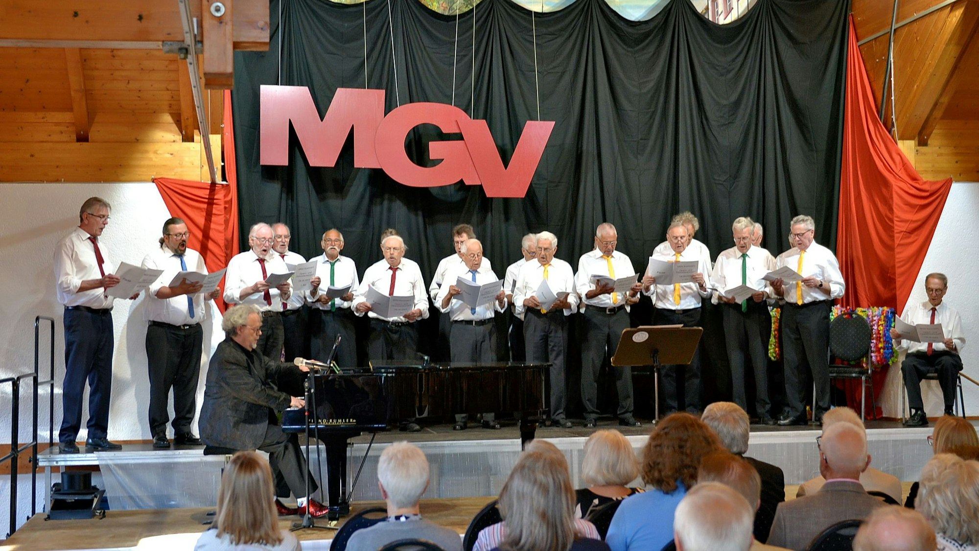 Die Sänger des MGV Kommern stehen auf der Bühne der Kommerner Bürgerhalle und singen.