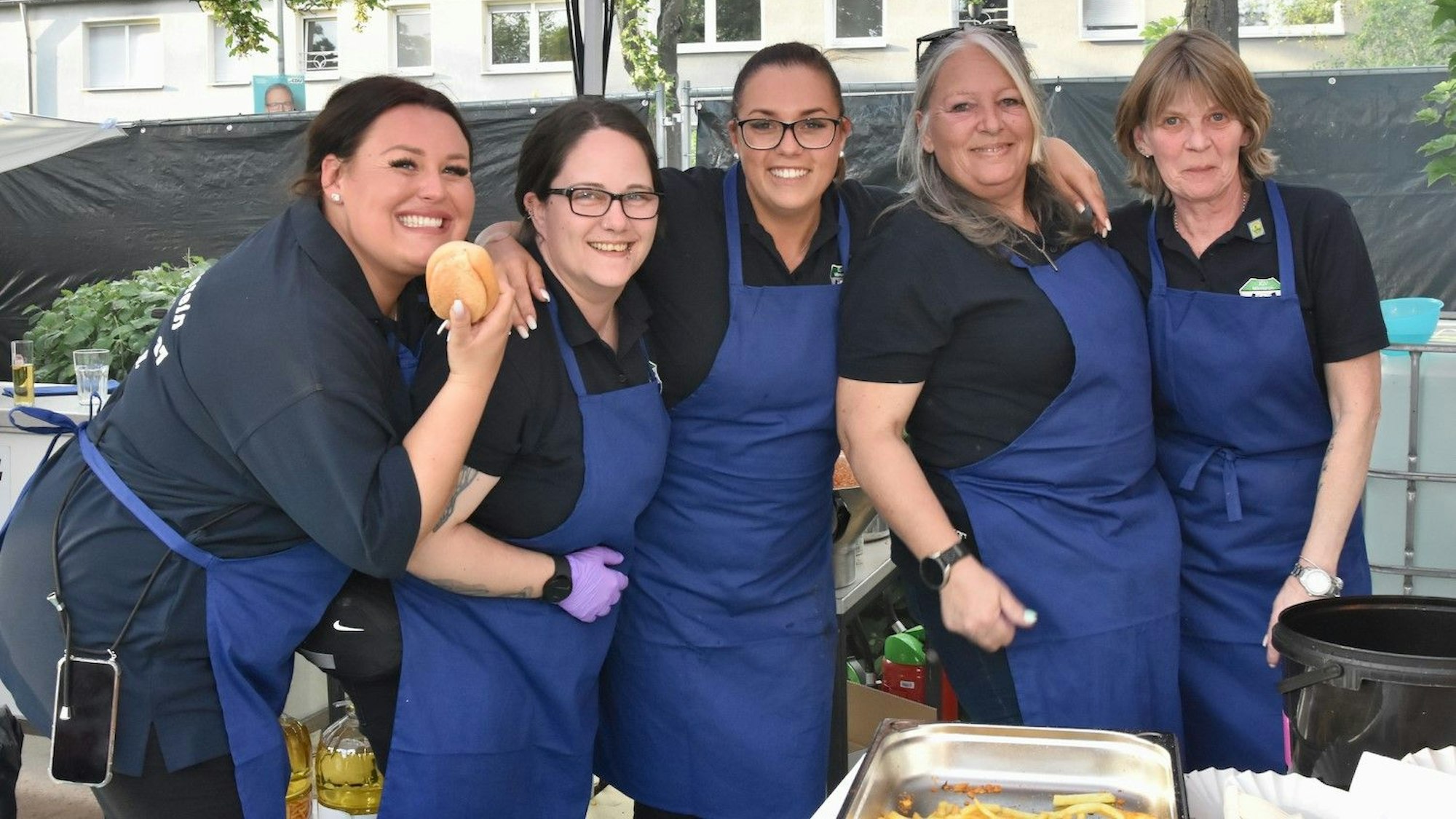 Mehrere Frauen mit blauen Schürzen stehen eingehakt.