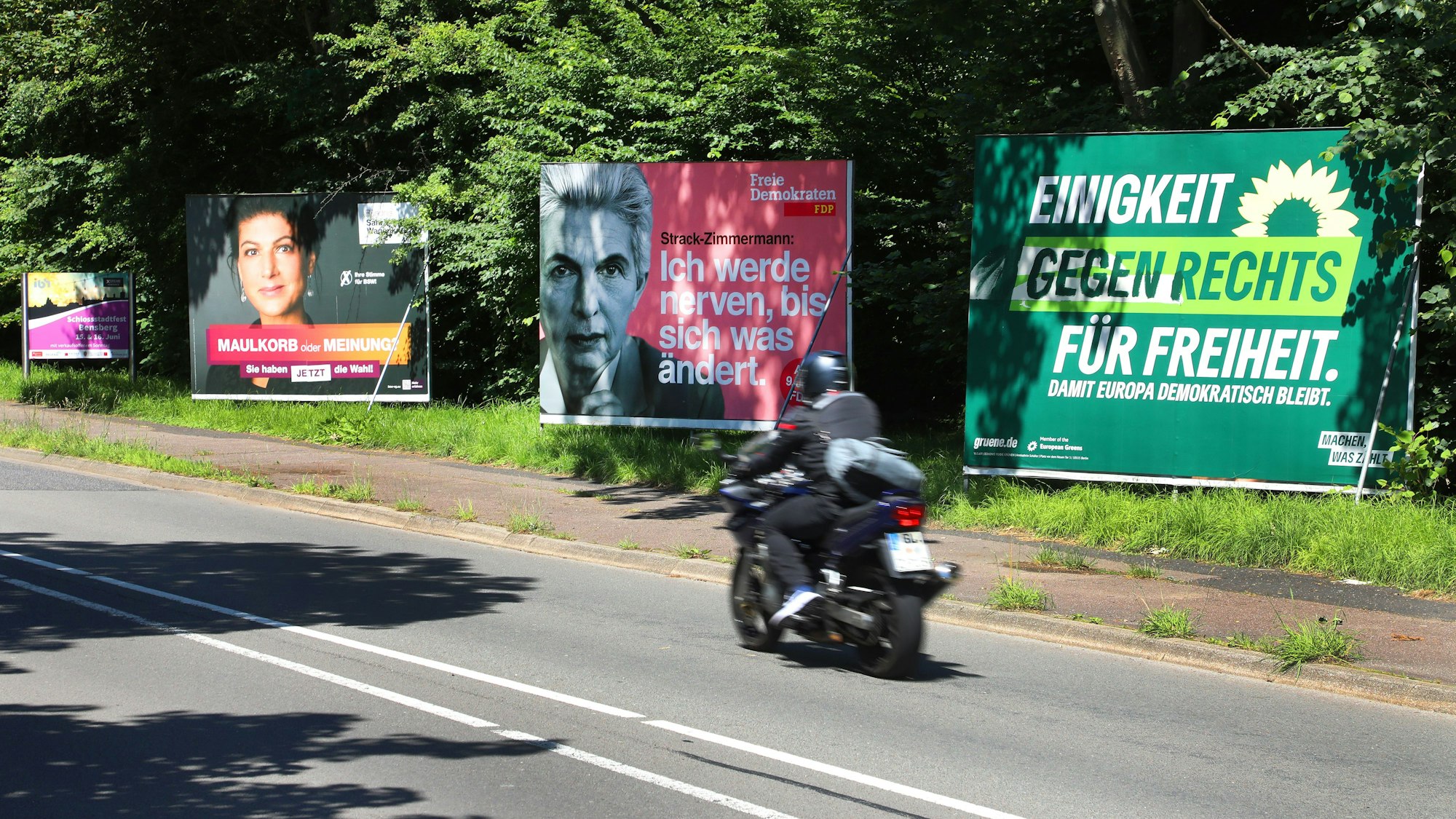 Wahlplakate stehen an der Overather Straße in Bergisch Gladbach-Bensberg. Auf dem Plakat der Grünen sind Schmierereien mit dem ursprünglichen Slogan wieder übermalt worden.
