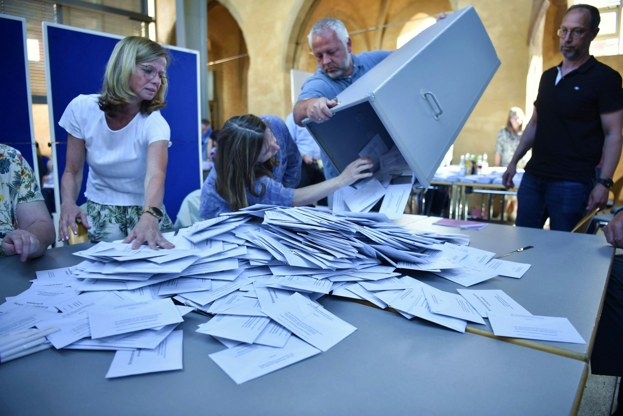 Wahlhelfer bei der Arbeit: Ein Mann entleert die Wahlurne auf einem Tisch, an dem die Stimmzähler warten.
