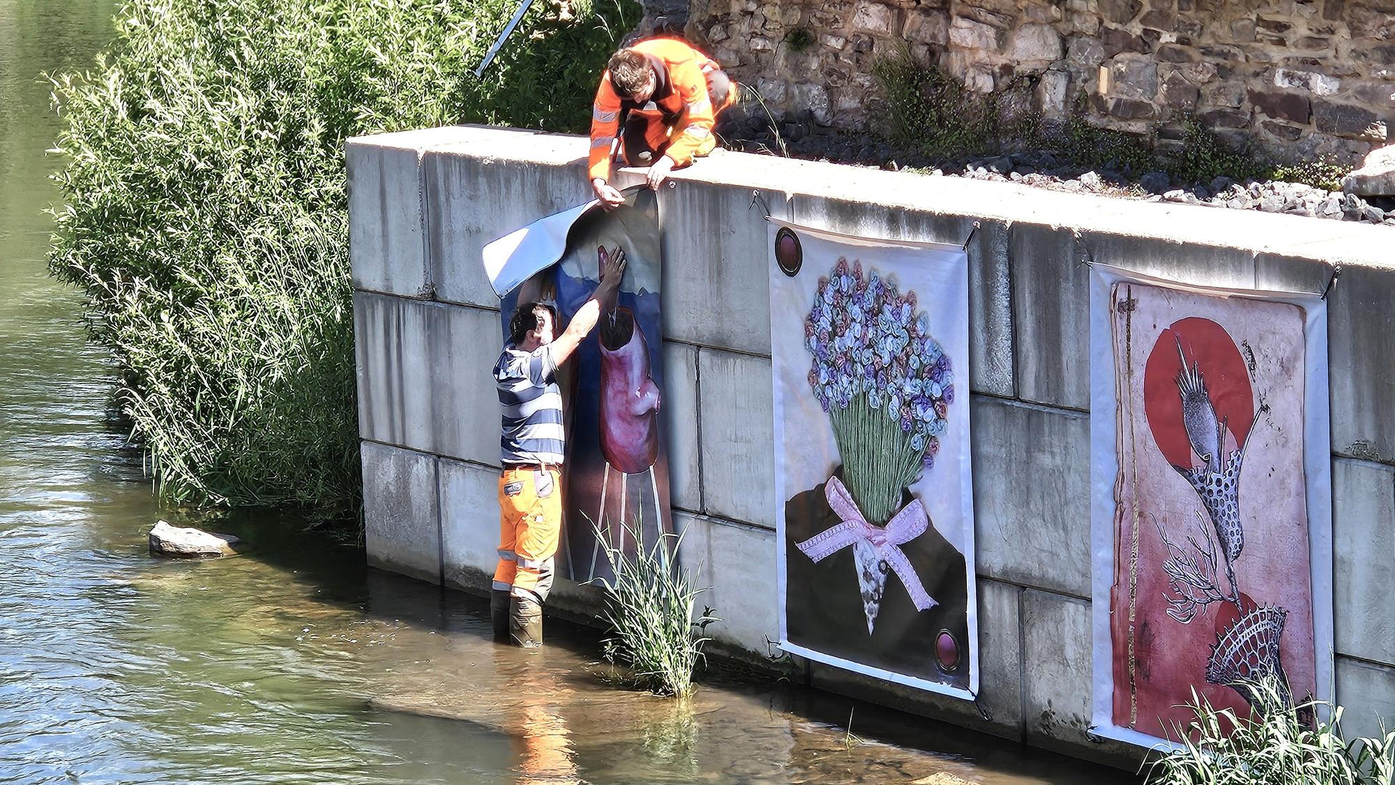 Zwei Arbeiter des Bauhofs bringen die Werke an der Mauer an.