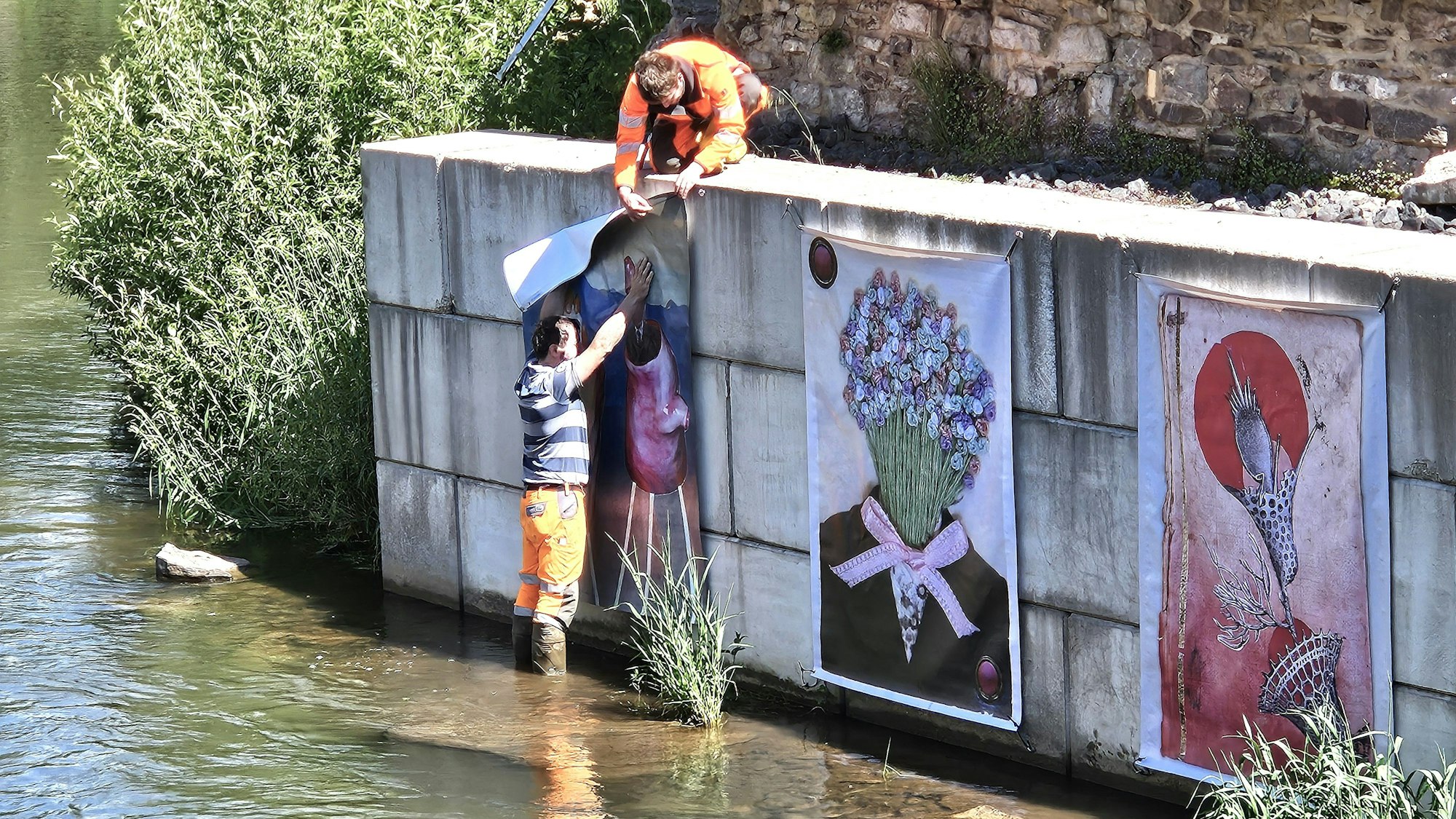 Zwei Arbeiter des Bauhofs bringen die Werke an der Mauer an.