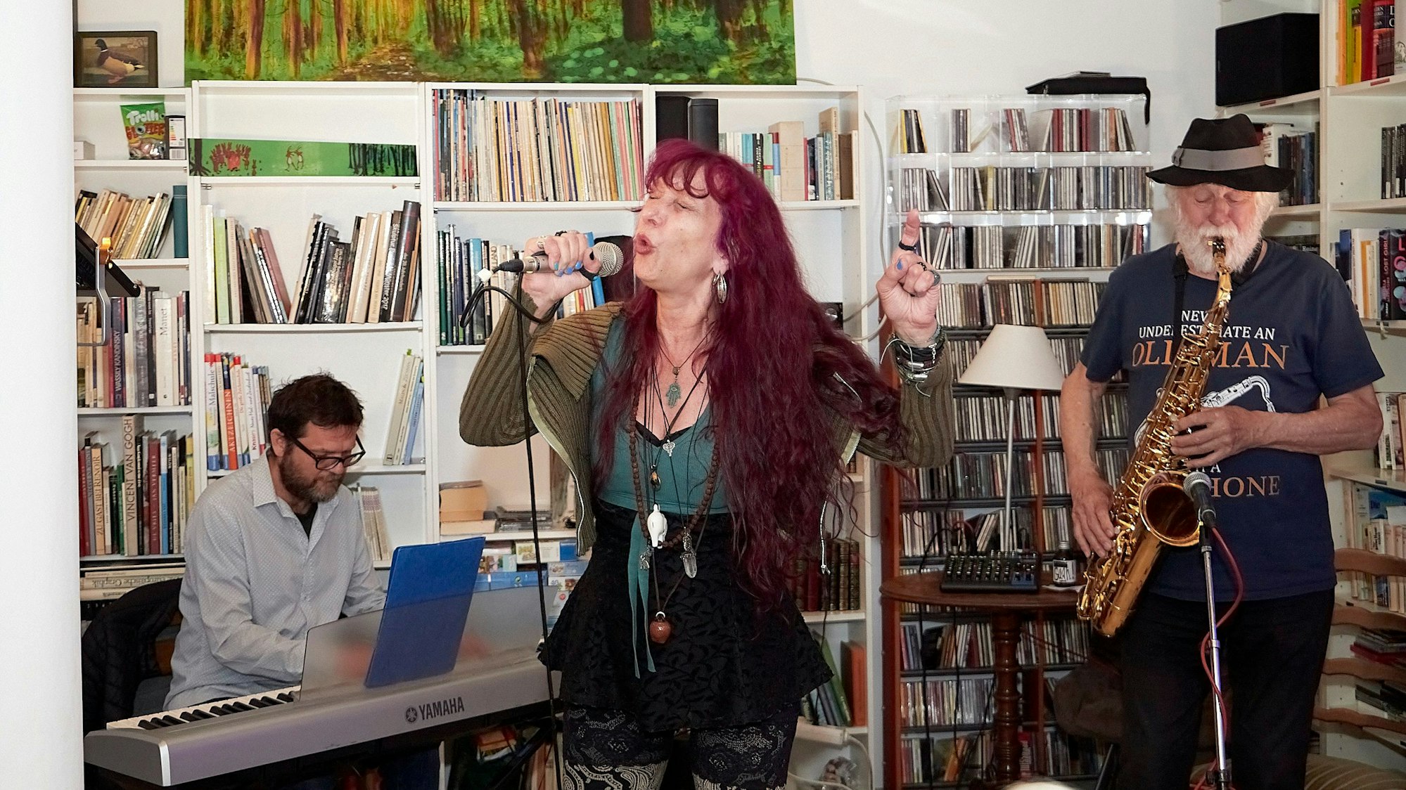 Sängerin Simone Reifegerste steht in der Bildmitte, sie hält ein Mikrofon in der Hand und singt. Rechts von ihr ist ein Mann zu sehen, der Saxofon spielt, links litzt ein Musiker an einem Keyboard.
