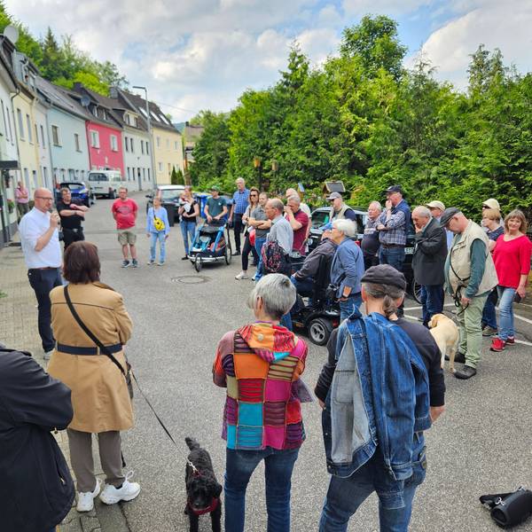 Bürgermeister Ingo Pfennings steht vor einem Haus in Gemünd und spricht in ein Mikrofon, die Teilnehmer des Spaziergangs stehen im Halbkreis vor ihm.