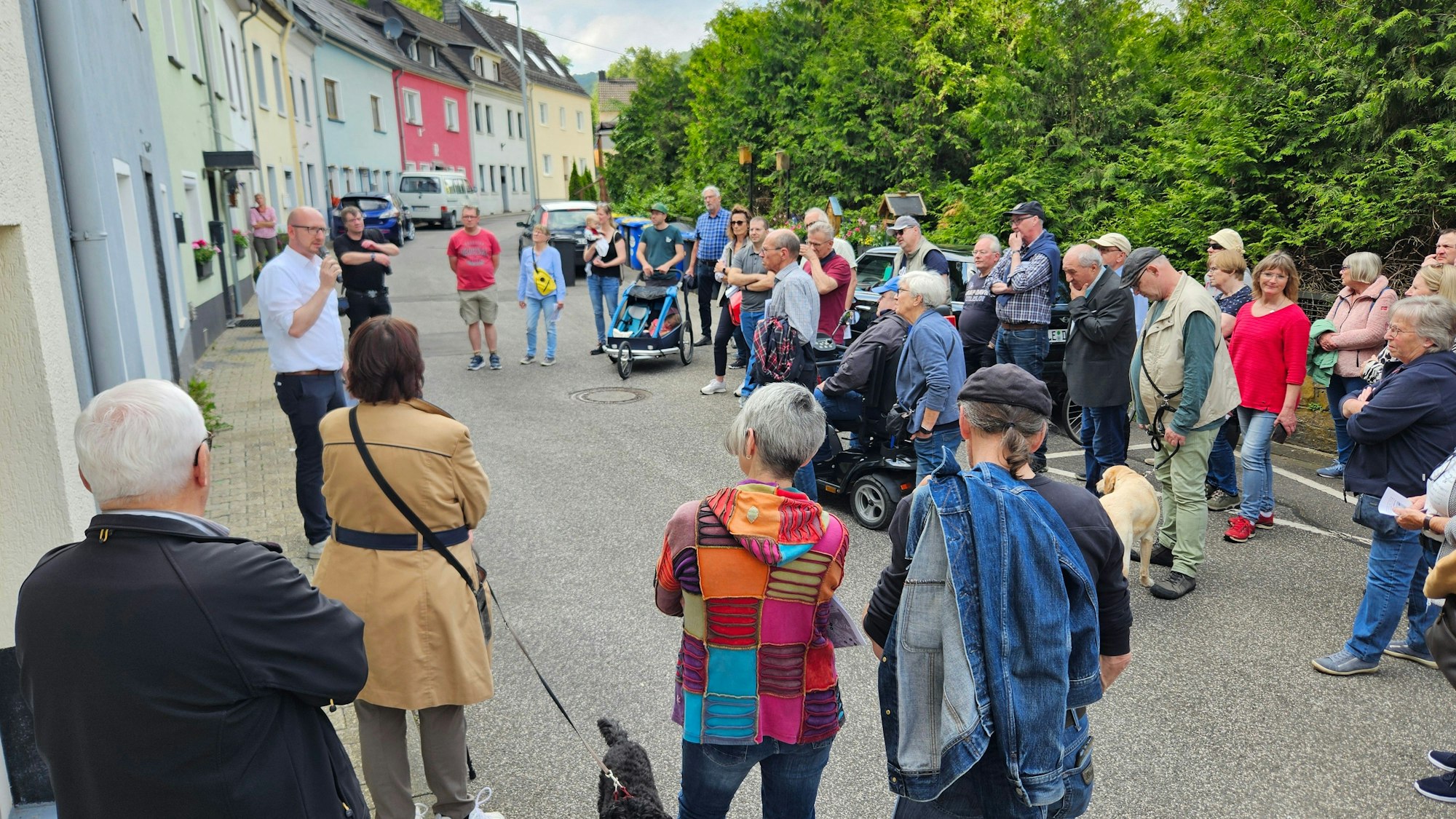 Bürgermeister Ingo Pfennings steht vor einem Haus in Gemünd und spricht in ein Mikrofon, die Teilnehmer des Spaziergangs stehen im Halbkreis vor ihm.