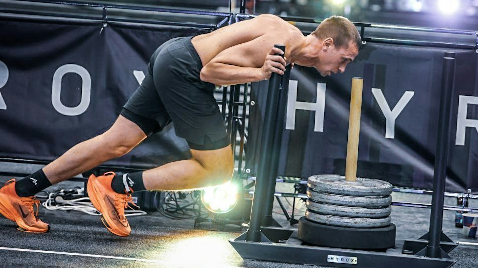 Roman Hopp, im Profil, schiebt den Hyrox-Schlitten, eine Metallplatte, die mit Hantelscheiben beladen ist.