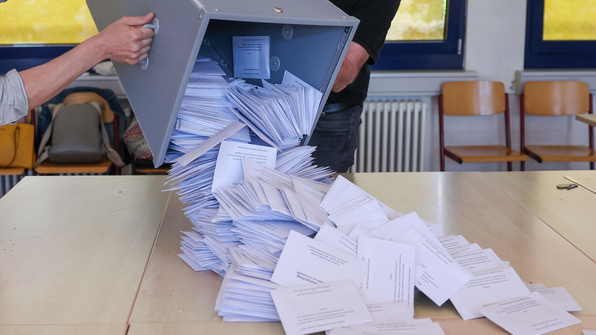 Zwei Wahlhelfer kippen eine Wahlurne mit den Briefwahlstimmen nach der Europawahl in einem Briefwahllokal zur Stimmenauszählung auf einen Tisch.