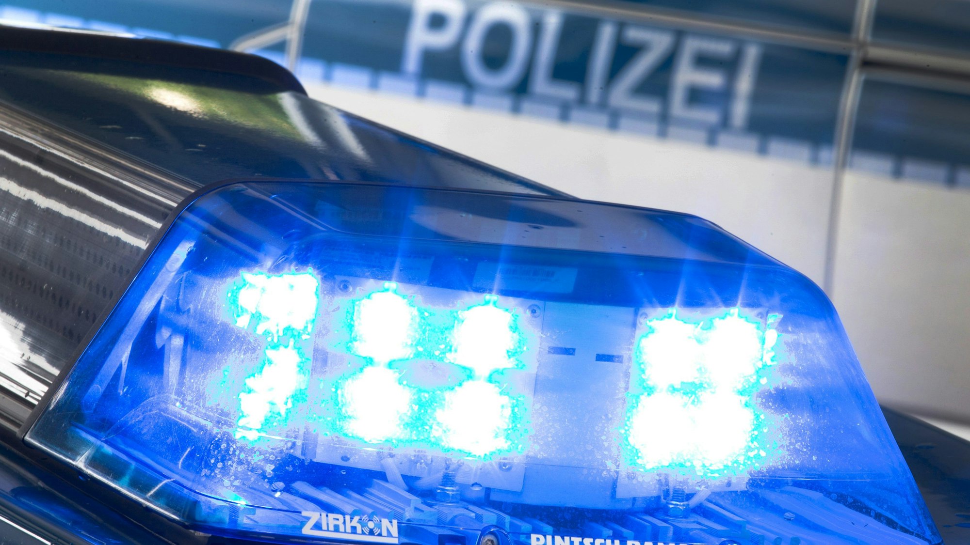 Ein Blaulicht leuchtet auf dem Dach eines Polizeiwagens. Im Hintergrund steht ein weiterer Streifenwagen.