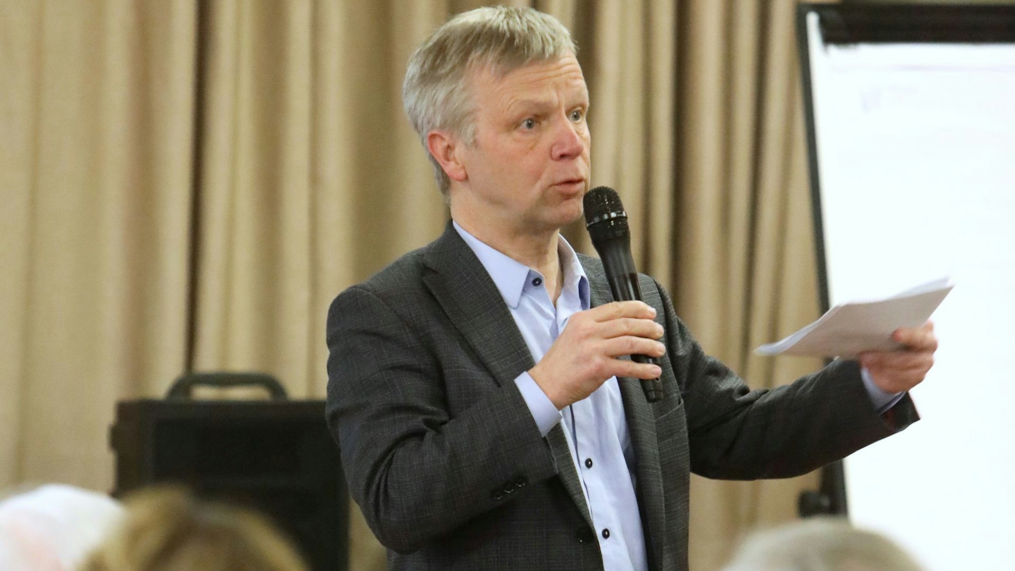 Ein Mann spricht in ein Mikrofon und hält Papiere in der Hand.