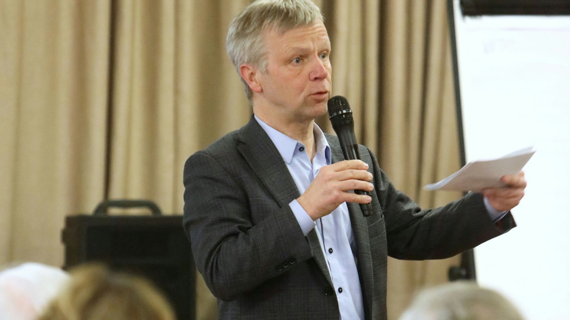 Ein Mann mit einem Mikrofon und einem Zettel in den Händen.