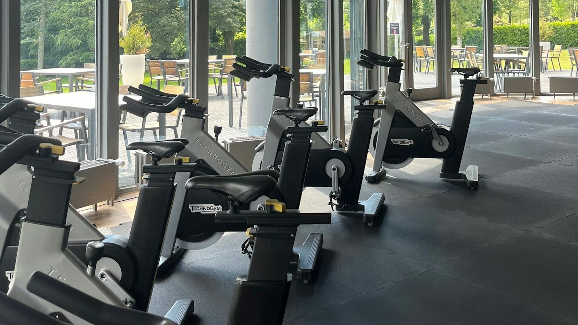 In einem Raum mit Blick auf eine Terrasse stehen Fitnessgeräte