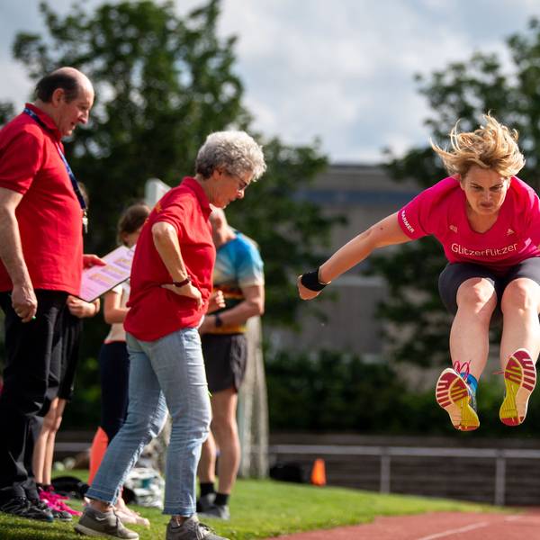 Ein Weitspringerin mitten im Sprung. Sportwarte kontrollieren die Absprungmarkierung.