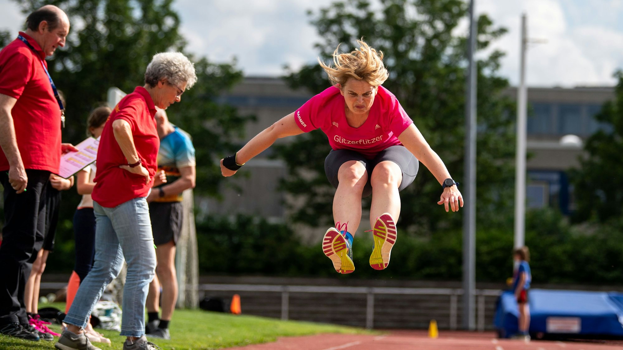 Ein Weitspringerin mitten im Sprung. Sportwarte kontrollieren die Absprungmarkierung.
