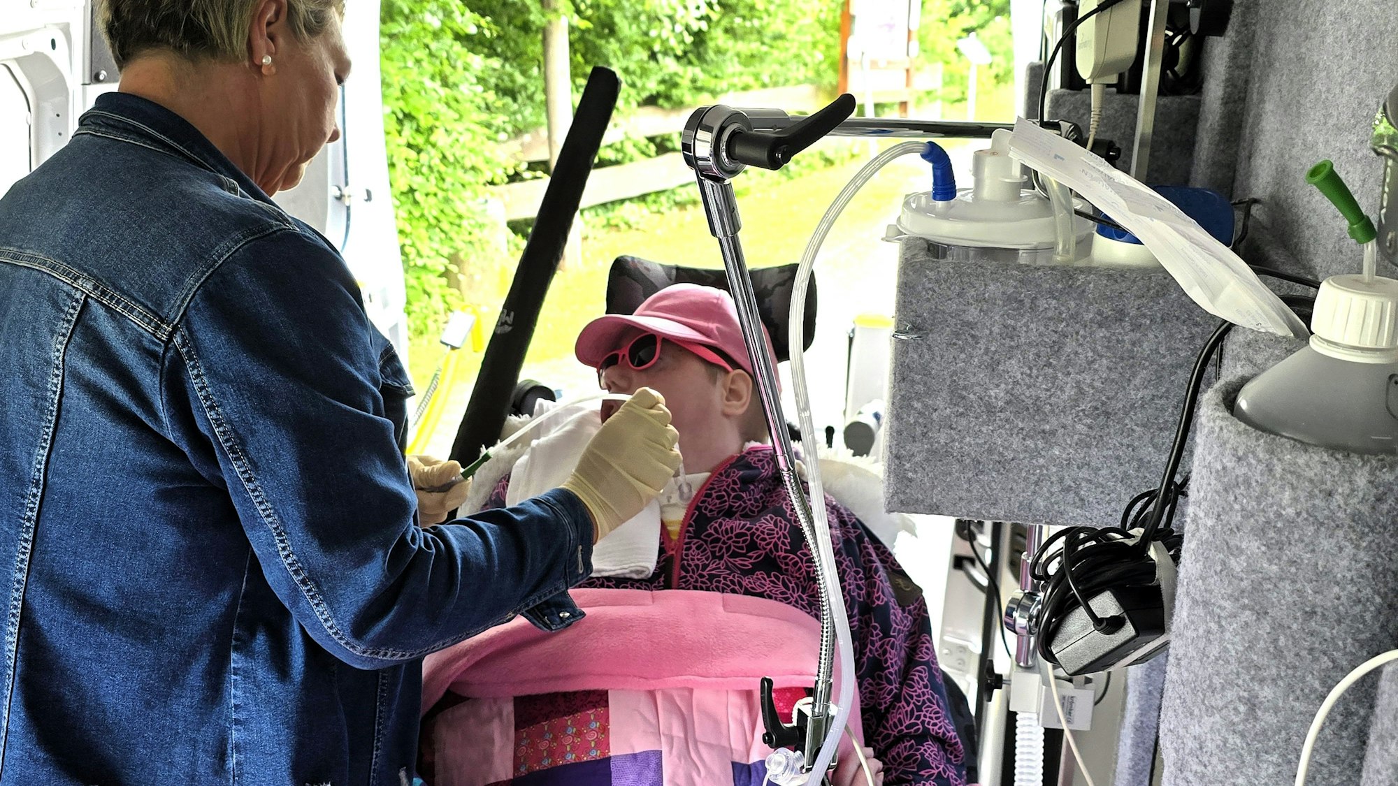 Eine Pflegekraft betreut in einem speziell umgebauten Transporter eine junge, schwerstbehinderte Frau.