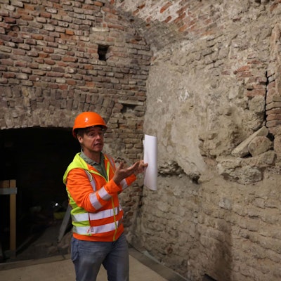 Ein Mann mit Bauhelm steht vor einer Mauer.