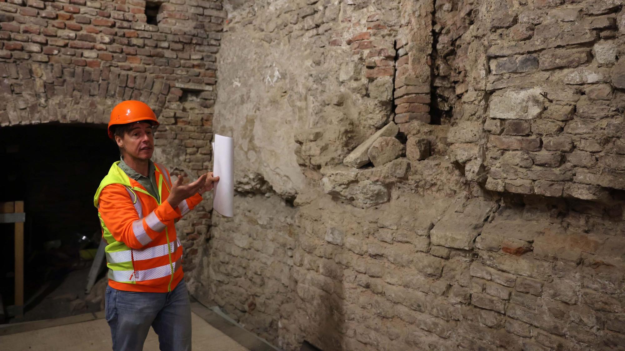 Ein Mann mit Bauhelm steht vor einer Mauer.