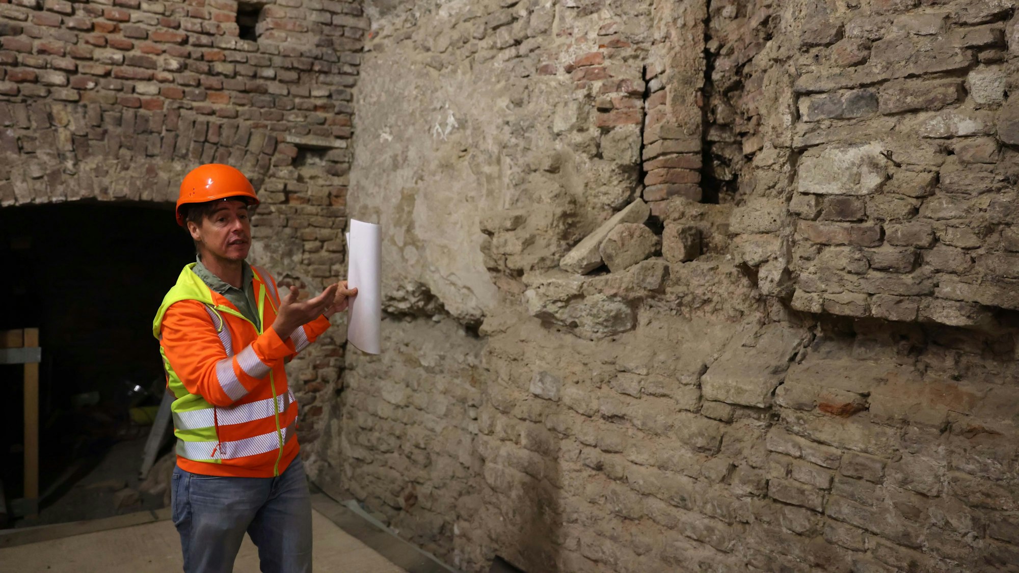 Ein Mann mit Bauhelm steht vor einer Mauer.