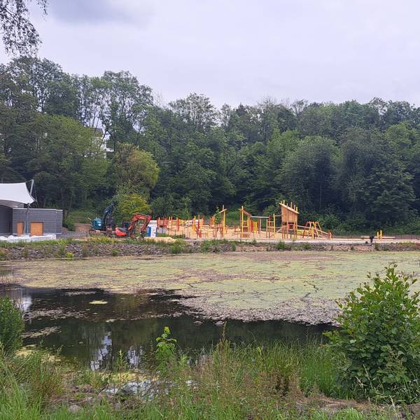 Das Foto zeigt den Heilteich und im Hintergrund den neuen Pavillon und den Spielplatz.