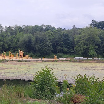 Das Foto zeigt den Heilteich und im Hintergrund den neuen Pavillon und  den Spielplatz.