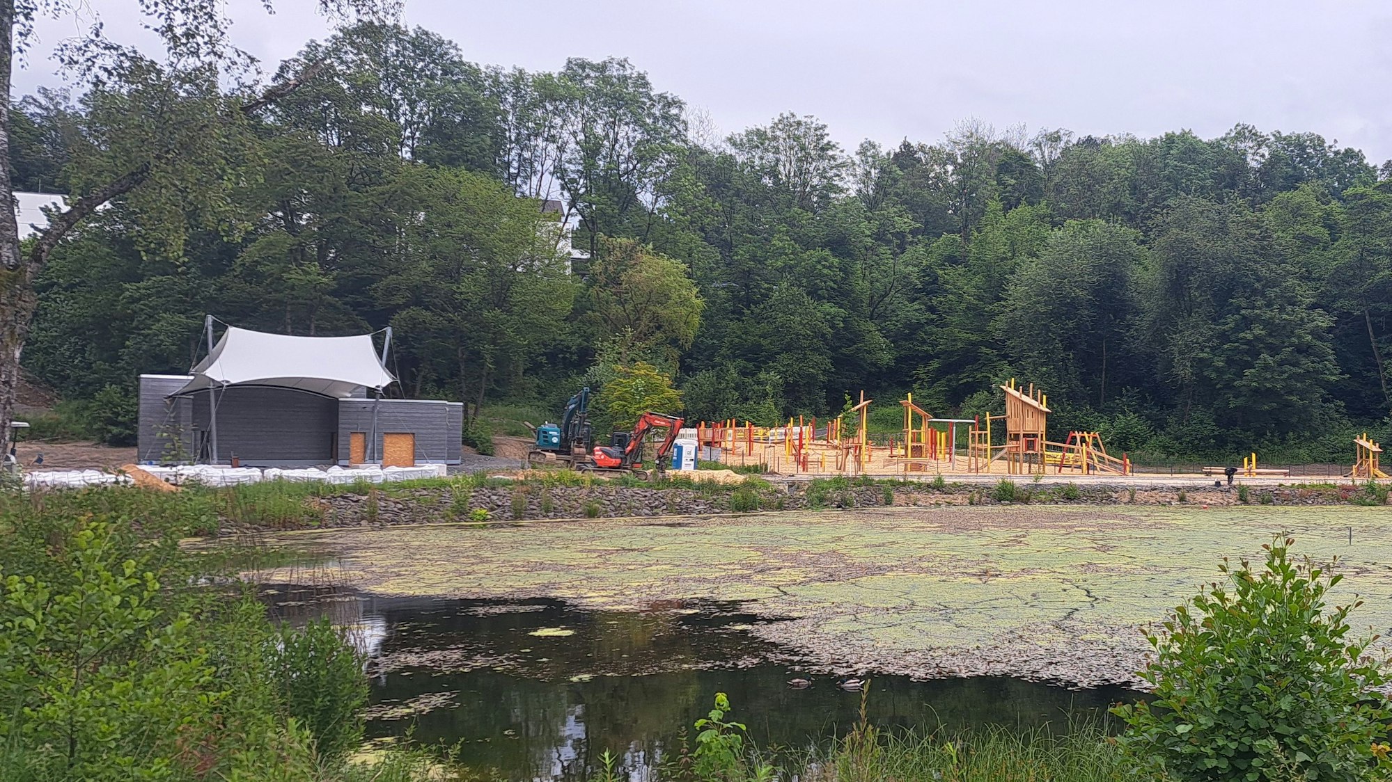 Das Foto zeigt den Heilteich und im Hintergrund den neuen Pavillon und den Spielplatz.