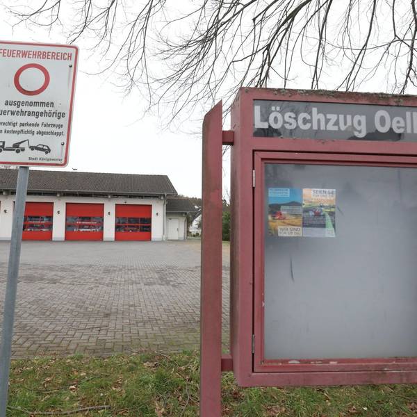 Ein leerer Schaukasten mit der Aufschrift Löschzug Oelberg, im Hintergrund das Gerätehaus mit vier roten Rolltoren.