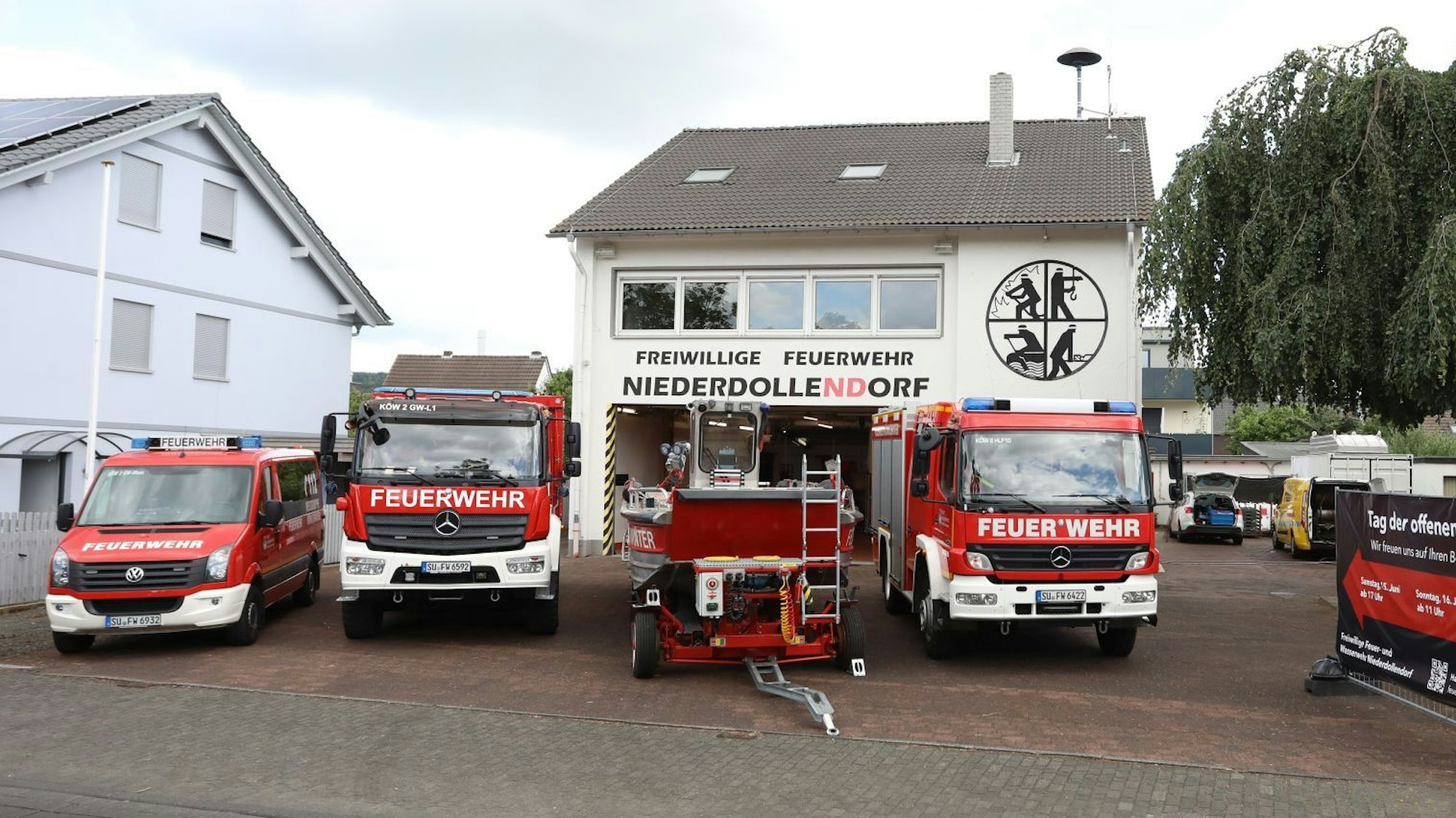 Einsatzfahrzeuge der Feuerwehr und ein Boot stehen vor einem Gerätehaus.