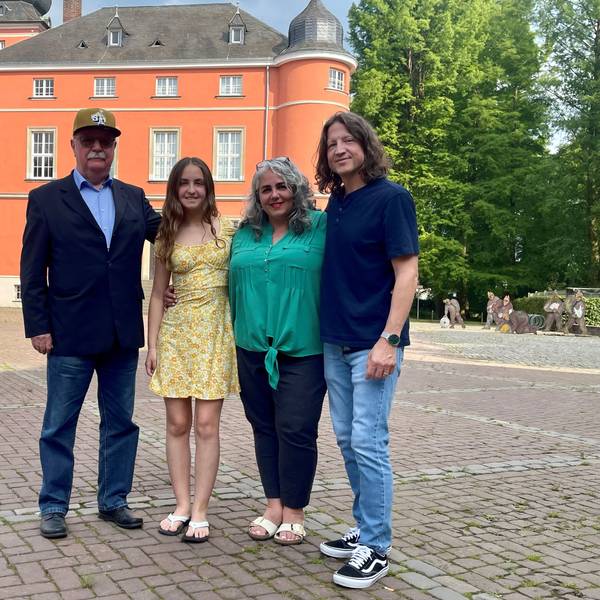 Zwei Männer und zwei Frauen stehen auf einem gepflasterten Hof.