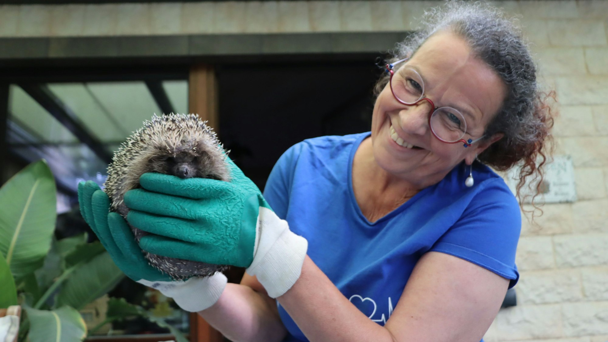 Eine lächelnde Frau hält einen Igel. Sie trägt Handschuhe.