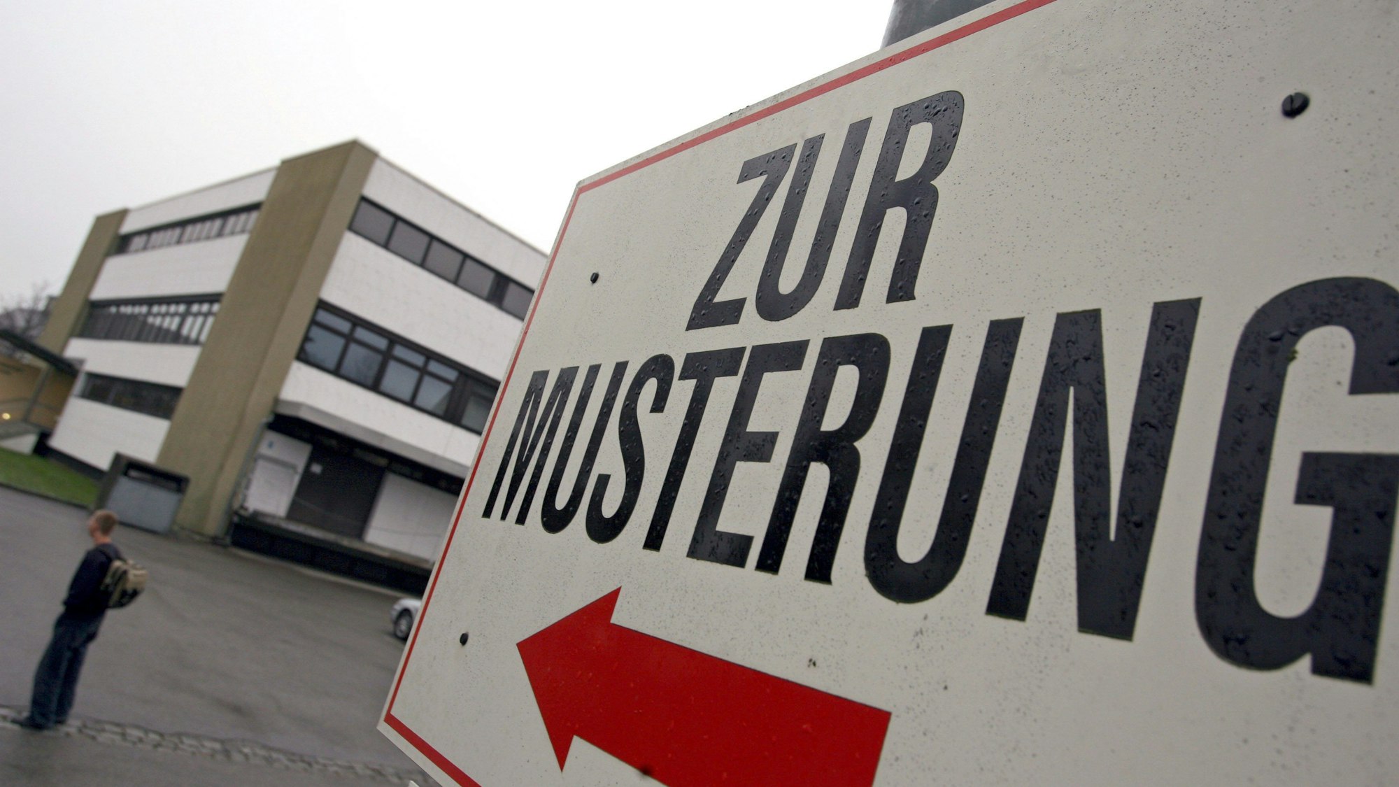 Ein Wehrpflichtiger steht unter einem Hinweisschild mit der Aufschrift „Zur Musterung“ vor dem Kreiswehrersatzamt.